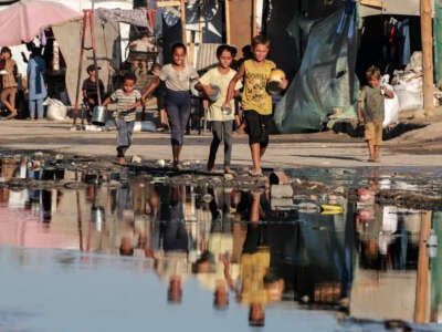 Palestinian children carrying empty containers walk near stagnant wastewater, on their way to a food distribution point in Deir el-Balah in the central Gaza Strip on July 19, 2024.